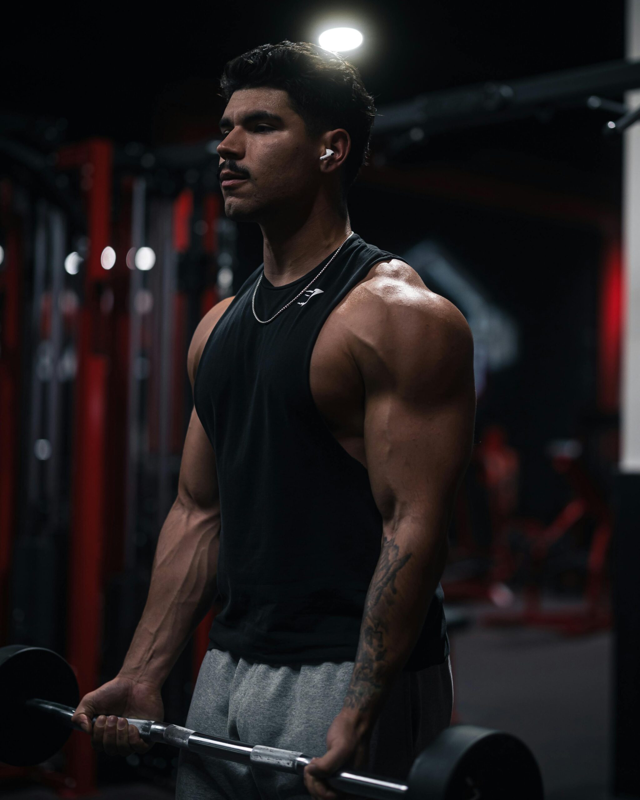 Strong male bodybuilder lifting dumbbells in a dark gym setting.